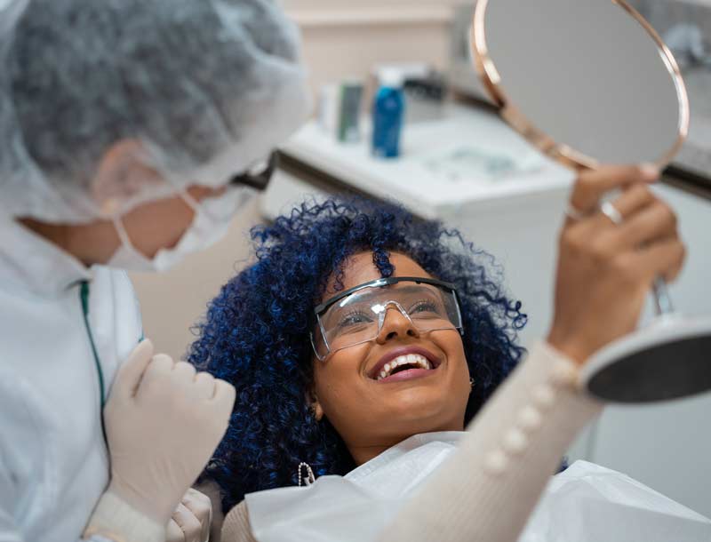 Woman smiling in mirror while in dentist chair