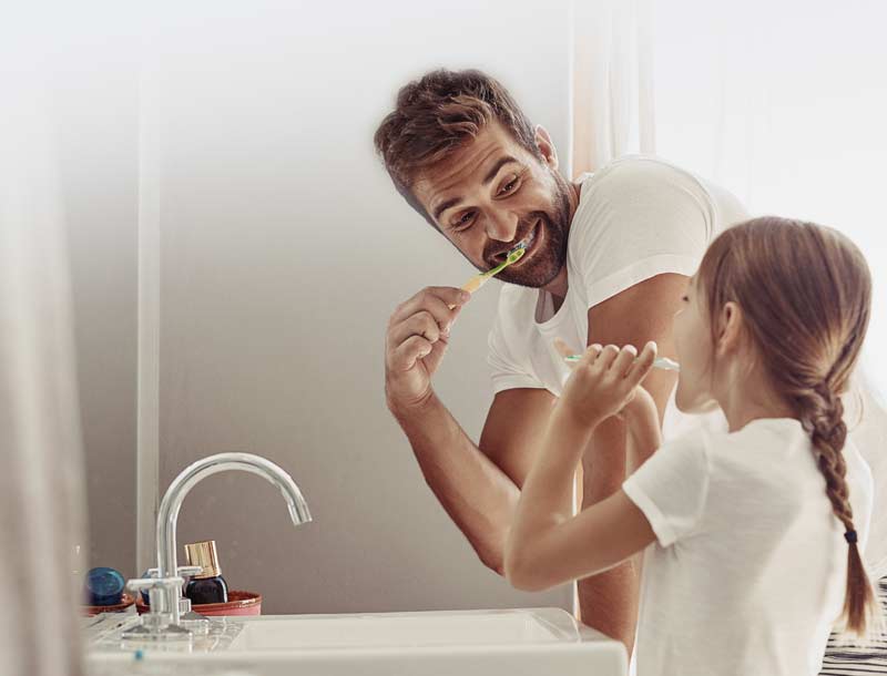 Father brushing teeth with daughter